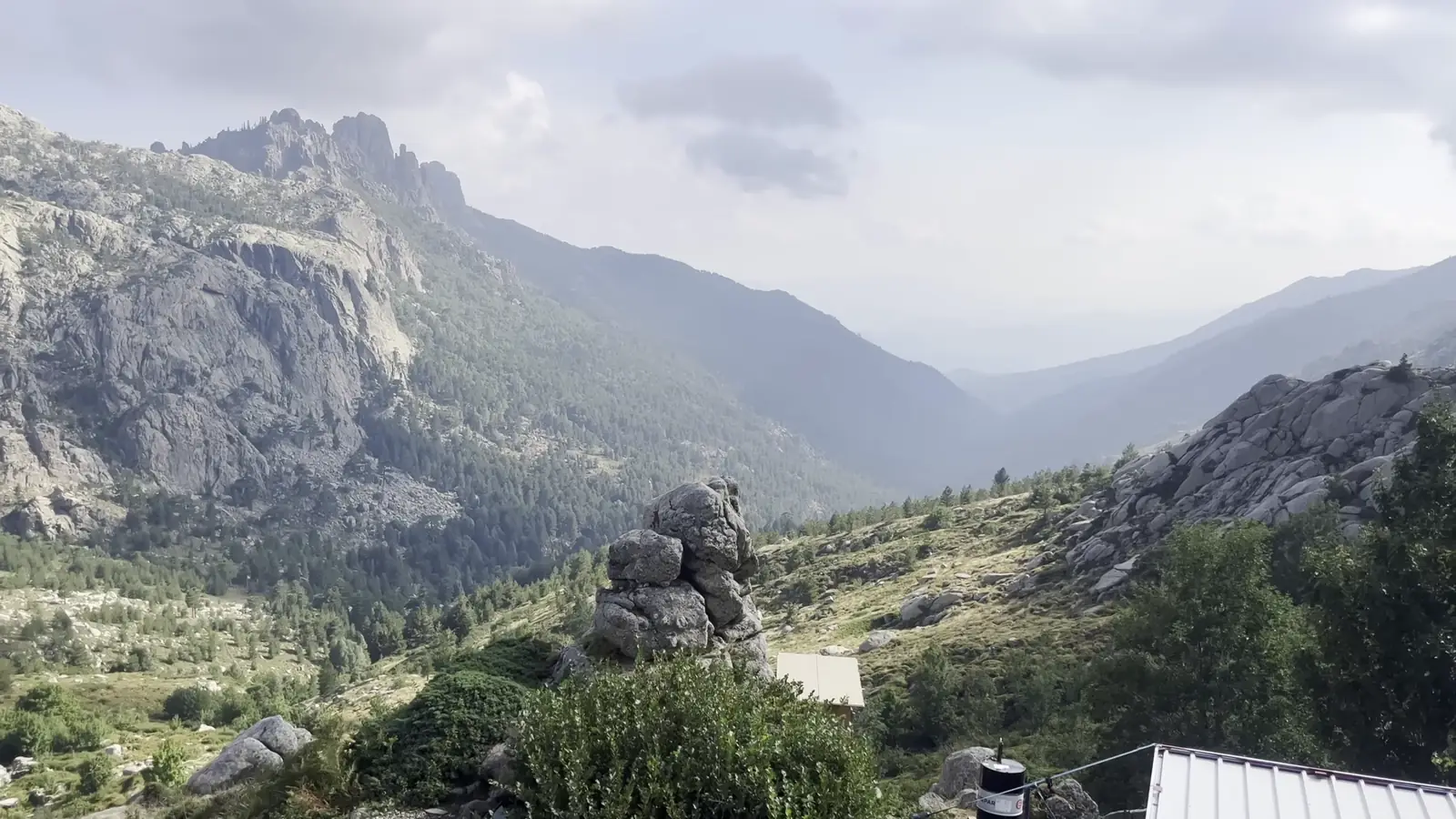 Toit du refuge d'Asinau, vallon boisé et premières aiguilles de Bavella dans la brume